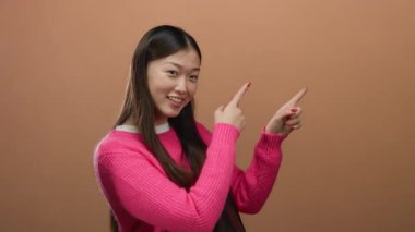 Kahverengi arka planda pembe süveter giyen, gülümseyen bir kadın.