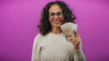 Rusya 'nın ruble banknotlarını elinde tutan kadın canlı mor bir arkaplan ile finans ve para birimi temalarını özgüvenli bir ifadeyle sergiliyor..