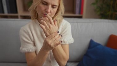 Evdeki kanepede oturan, el ele tutuşan, rahat oturma odasında rahatlarken, rahat olmayan, kitaplarla ve dekorla çevrili, gündelik süveter giyen bir kadın..