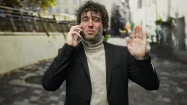 Genç adam şehrin dışında bir telefonda konuşurken el sallıyor, samimi bir jest ve hareketli bir sokak arkaplanıyla kentsel bir anı yakalıyor..