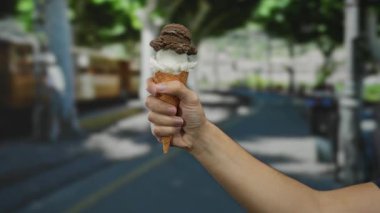 Elinde çikolatalı ve vanilyalı dondurma külahı olan bir adam şehrin arka planında ve güneşli bir havada yaz havasını yakalıyor..