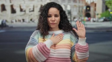 Roma Kolezyumu 'nda yemin eden bir kadın, tarihi arkaplanda renkli bir süveter giyiyor, açık havada ikonik bir turistik bölgede vaatte veya bağlılığa işaret ediyor..