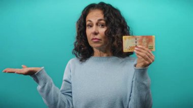 Güney Afrika banknotlarını elinde tutan orta yaşlı bir kadın mavi arka planda kararsız bir hareketle.