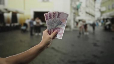 Yoğun bir şehir caddesinde elinde Türk lirası banknotları tutan adam, finansal kavramları ve şehir yaşamını ön plana çıkarıyor..