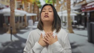 Şehir sokaklarında duygularını ifade eden beyaz tişört giyen bulanık şehir geçmişine sahip düşünceli bir kadın.