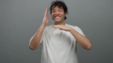 Beyaz gömlekli İspanyol bir adam gri bir arka plana gülümsüyor, bir stüdyo ortamında neşeli ve kendinden emin bir tavır yakalıyor..