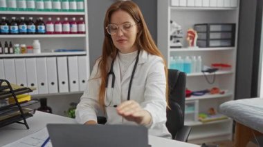 Klinikte çalışan bir kadın dizüstü bilgisayarla çevresi tıbbi malzemeler ve ciltlerle çevrili profesyonel bir sağlık hizmeti ortamı sergiliyor..