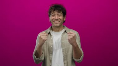 Heyecandan gülümseyen yakışıklı bir adam canlı pembe arka planda neşeli ve mutlu bir ifade sergiliyor.