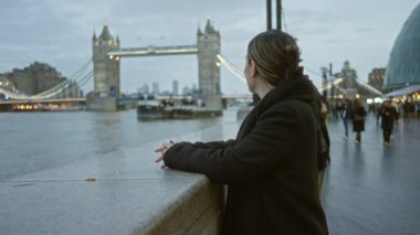 Akşamları Londra 'daki Tower Bridge manzarasından hoşlanan bir kadın, arka planda şehir manzarası, şehir yaşamını ve seyahatleri simgeliyor..