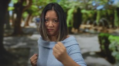 Parkta dövüş sanatları uygulayan genç bir kadın, gücünü sergiliyor ve sakin açık hava ortamının ortasında, dinamik hareketini ve yoğunluğunu doğal ortamında yakalıyor..