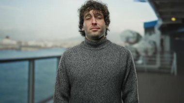 Gri kazaklı genç adam deniz kenarındaki bir limana yakın bir yerde parmakları kafaya bir jest yapıyor, bulanık bir geçmişi olan bir teknede düşünceli bir anı yakalıyor..