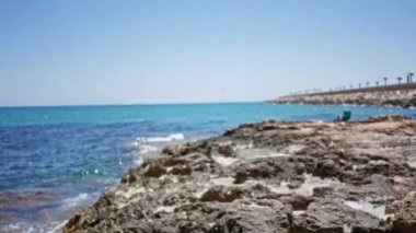 Bulanık deniz manzarası, kayalık kıyı ve turkuaz okyanus, parlak mavi gökyüzünün altında.