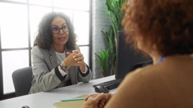 Doğal ışık ve bilgisayarlarla modern bir ofiste iş tartışan kadınlar, mesleki ortaklık ve iletişim becerilerini vurguladılar.