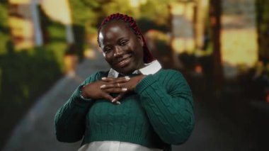 Güneşli bir parkta yeşilliklerle eğlenen, rahat bir kazak giyen, neşeli ifadesi ve açık havada yaptığı hareketlerle mutluluğu ve kendine güveni gösteren bir kadın..