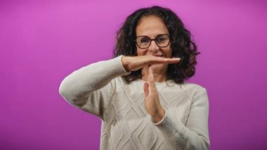 Kıvırcık saçlı ve gözlüklü bir kadının canlı mor arka plana karşı jest yapması duraklama ve gevşeme kavramını ortaya koyuyor..