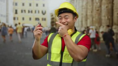 Miğfer ve çelik yelek giyen adam işlek şehirde gülerken elektronik sigara tutuyor..
