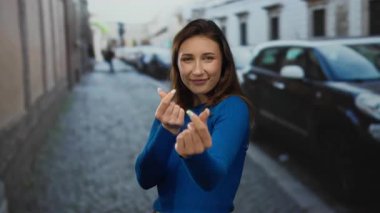 Mavi kazaklı genç bir kadın park etmiş arabalarla şehir caddesinde parmakları olan kalp sembolleri yapıyor..