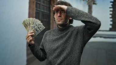 Şehir sokaklarında İspanyol bir adam heyecanla Amerikan doları banknotlarını tutarken şehir mimarisinin arka planıyla gözlerini kısıyor..