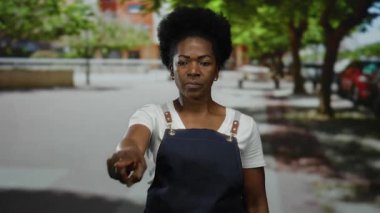 Yapraklı ağaçlar ve şehir manzarası ile çevrili, güneşli şehir caddesini işaret eden önlüklü kadın şehir merkezini kapsıyor..