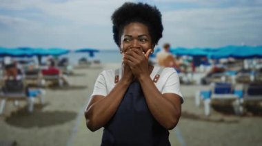 Deniz kenarındaki önlüklü kadın, elleri mavi şemsiyelerin altında ve açık gökyüzünde açık havada doğal bir anı yakalıyor..