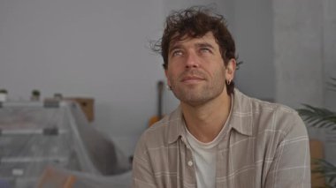 Yeni bir evde gülümseyen İspanyol adam rahat ve minimalist oda ortamında mutluluk ve beklenti anı yakalıyor..