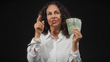 Şili pesolarını kara fon üzerinde tutan kadın, mali bağlamda düşünceli düşüncelerini dile getiriyor, para ve karar verme konusunda orta yaşlı endişelerini vurguluyor.