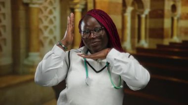 Steteskoplu kendinden emin bir kadın kilise ortamında gülümsüyor, elleriyle çerçeve hareketi yapıyor, gözlük takıyor, sağlık ve maneviyat bağlantısını tasvir ediyor..