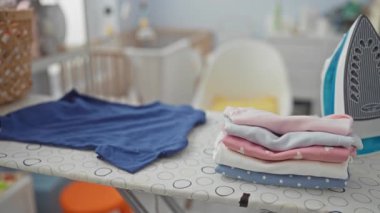 Kadın, rahat çamaşır odasında, ütülenmiş giysiler ve ön planda ütü masasıyla rahatlıyor..