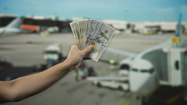 Bir havaalanı terminalinde arka planda görünen bir uçakla el ele tutuşmak seyahat masraflarını ve finansal planlamayı öneriyor..