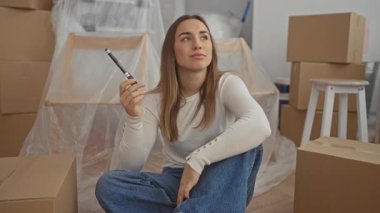 Yeni dekore edilmiş bir evin içinde kutuları taşırken fikirleri düşünen bir kadın, yaratıcılığını ve gelecekteki ev düzenlemeleri ve iyileştirmeleri için planlar yapıyor..