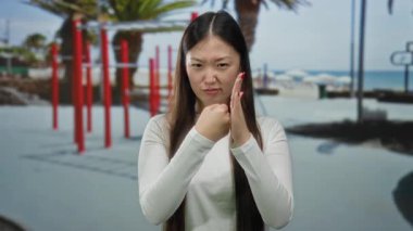 Spor salonunda arka planda palmiye ağaçları olan bir kadın egzersiz ortamında yumruğunu sıkarken azim ve odaklanma gösteriyor..