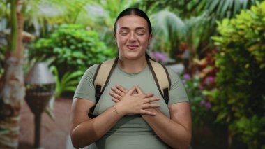 Güneşli bir parkta gülümseyen ve eğlenen bir kadın canlı yeşil bitkilerle çevrili, doğanın güzelliğini kucaklarken mutluluk ve sükunet saçıyor.