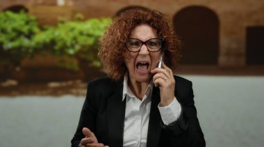 Kadın cep telefonuyla bağırıyor, şehrin arka planında duygularını ve aciliyetini yakalıyor..