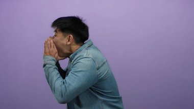 İzole bir mor arka plan duvarına bağıran genç adam, günlük kostüm içinde duygularını ve enerjisini ifade ediyor, iletişimi ve canlılığı iletiyor..