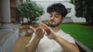 Güneşli bir günde açık havada el kol hareketi yapan sakallı genç bir adam yaz atmosferinde duygularını dışa vuruyor..