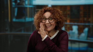 Otelde gizlice fısıldayan kadın, etkileyici bir jestle orta yaş ve kapalı mekan hikayeleri için sürpriz sevinç ortamı vurguluyor.