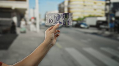 Elele tutuşan Kanada Doları banknotları, şehir arka planına dikkat çeken bir adamı gözler önüne seriyor ve her gün para birimini ön plana çıkarıyor..