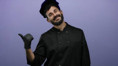 Siyah üniformalı ve eldivenli İspanyol sakallı şef mutfak sanatlarında profesyonellik gösteren canlı bir mor arka plan karşısında güvenle gülümsüyor..