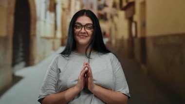 Sakin bir şehir caddesinde gülümseyen bir kadın gözlük takıyor ve parlak bir günde gri bir gömlek ve bulanık bir arka plan ile büyüleyici şehir mimarisi sergiliyor..