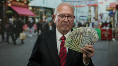 Kıdemli adam, renkli dükkanlar ve hareketli atmosferli şehir ortamında zenginlik ve iş başarısını ifade eden hareketli caddelerde bize dolar tutuyor.