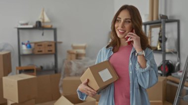 Yeni evdeki telefon kulübesinde konuşan bir kadın taşınma gününün rahat atmosferini gösteren bir apartmanın oturma odasında kutular ve raflarla çevrili..