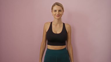 Pembe duvara karşı duran, siyah bluz giyen, sarı saçlı, kendine güvenen, izole edilmiş stüdyo resmi, gösterişli güzellik, genç görünümü, rahat poz veren kadın..