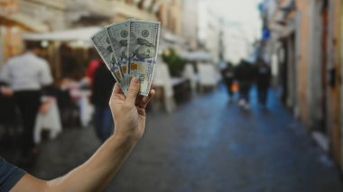 Kalabalık bir caddede Amerikan dolarlarını elinde tutan bir adam, şehir dışı şehir zeminine karşı kurulmuş, ekonomik işlemleri ve yaşam tarzı görüntülerini yakalıyor..