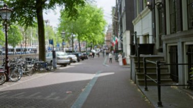 Amsterdam şehir manzarası bulanık yayalar, bisikletler ve arabalarla ağaçlarla gölgelenmiş bir cadde, Hollanda 'nın canlı kentsel özünü ve kendine özgü mimarisini yakalıyor.