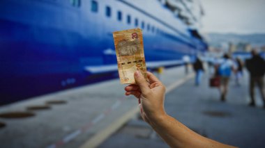 Elele tutuşan Güney Afrika rand banknotları bir limanın yakınındaki insanların yürüdüğü ve büyük bir teknenin yanaştığı, seyahat ve döviz kurunun özünü yakaladığı bir liman..