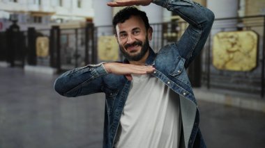 Sakallı İspanyol bir adam, güneşli bir günde neşe ve coşku ifade eden, arka planı bulanık kot ceketli, şehir sokaklarında heyecanlı bir şekilde el kol hareketi yapıyor..