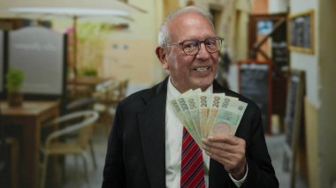 Üst düzey bir adam açık hava restoranının terasında Czech Koruna banknotları tutuyor. Canlı bir sokak ortamında iş başarısı sergiliyor..