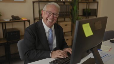 Ofisteki bir bilgisayarda çalışan takım elbiseli kıdemli bir adam profesyonel bir iş ortamını gösteriyor..