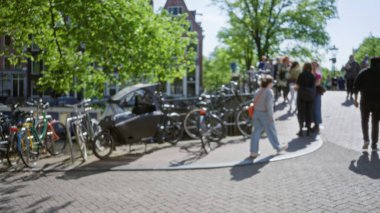 Arka planda bisiklet, insan ve ağaçlarla bulanık sokak manzarası güneşli bir günde sakin bir şehir havası yakalıyor..