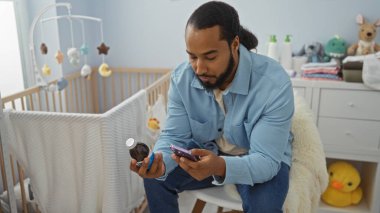 Genç adam yatak odasında sakallı bir şişe ve telefonla bebek odasında beşik, iç mekan, oyuncaklar ve mobilyalarla oturuyor.